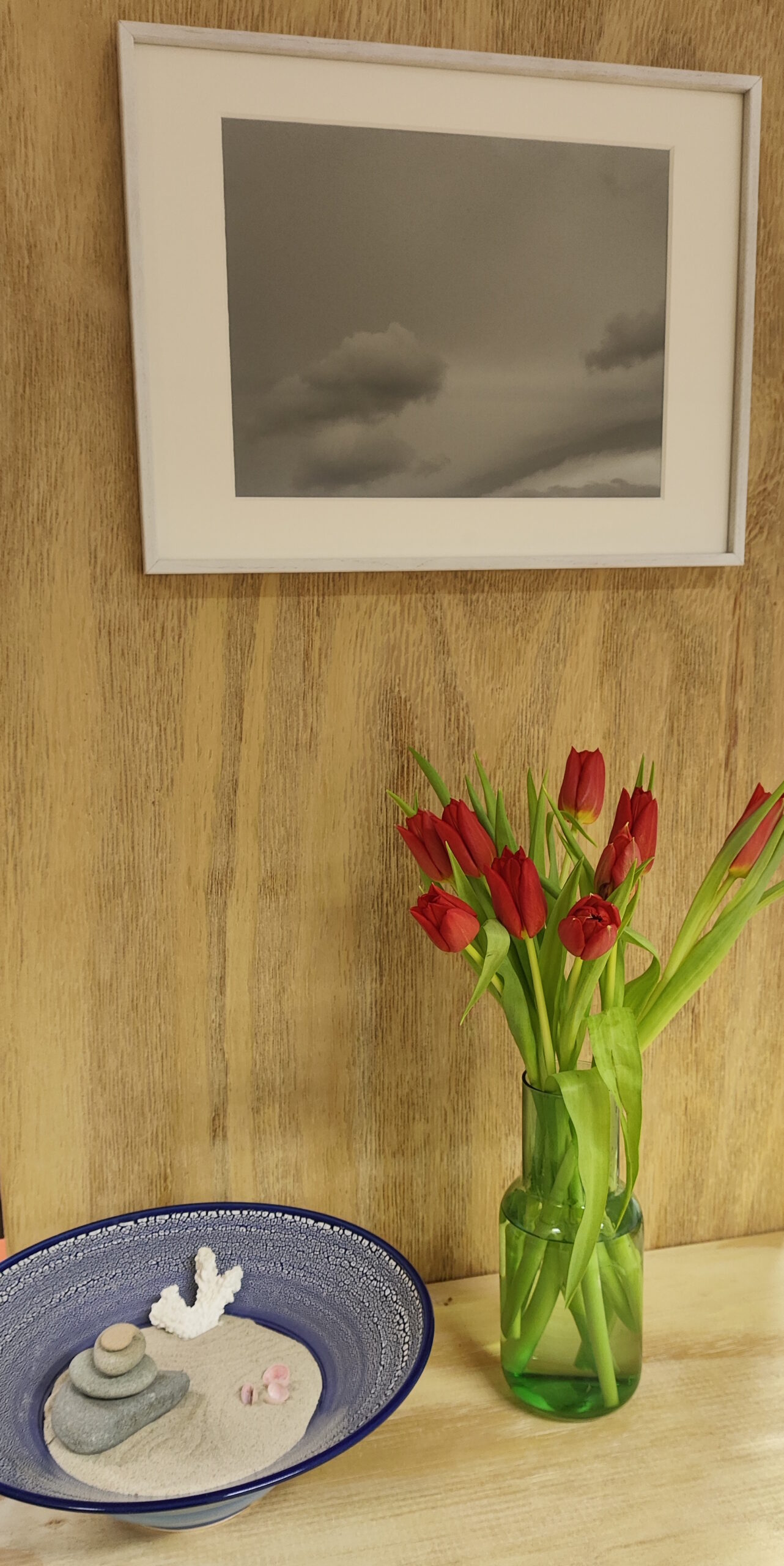 Eine Schale auf einem Holzregal. Daneben eine Vase mit roten Tulpen und darüber ein Bild