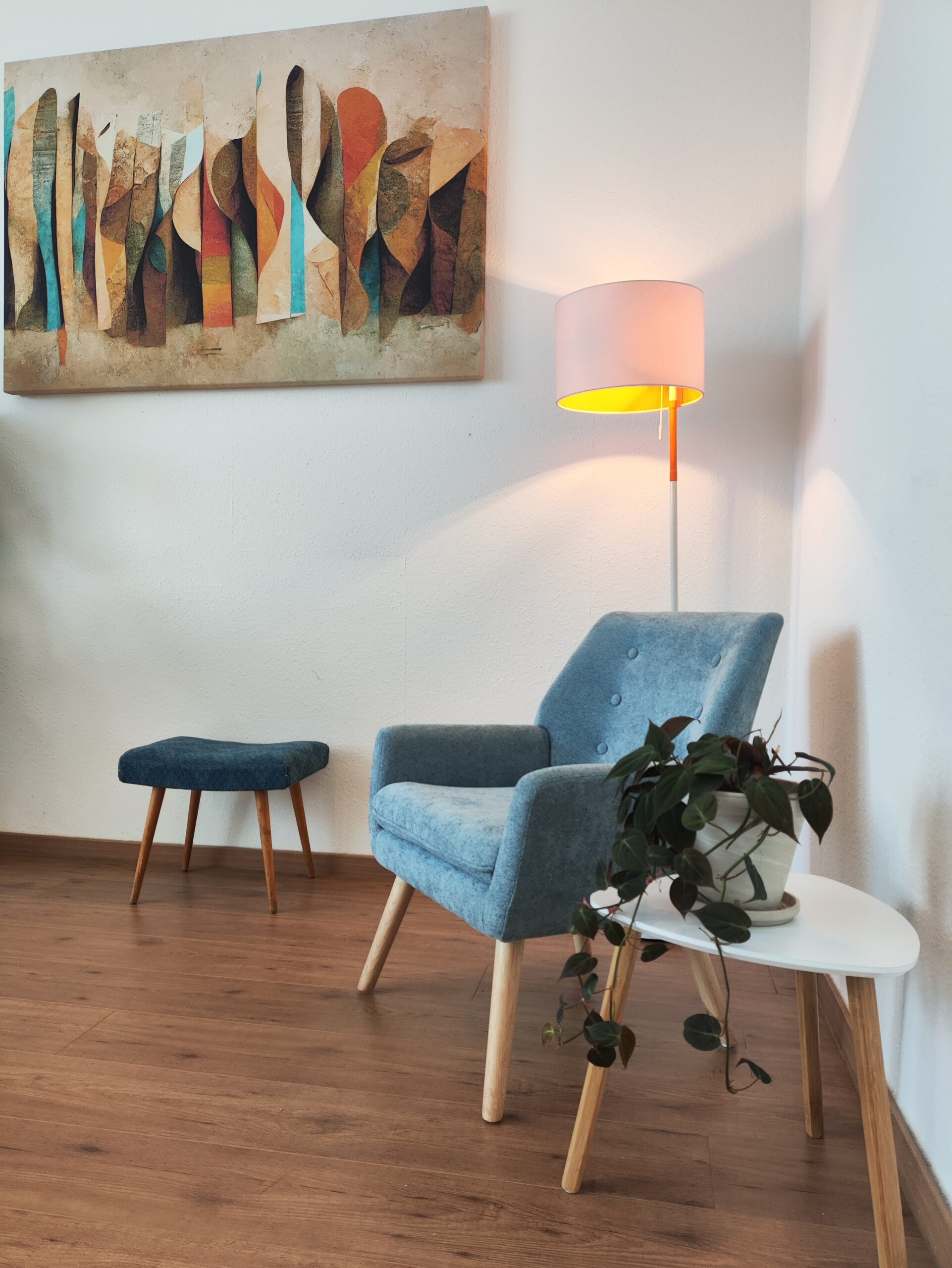 Ein Stuhl in einer gemütlichen Ecke mit einem Tisch daneben und einer Stehlampe dahinter. An der Wand hängt noch ein Bild