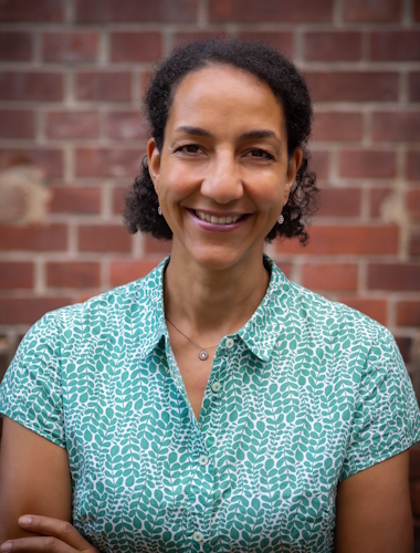 Sinidu Deneke lächelnd in einem Kleid vor einer Backsteinmauer