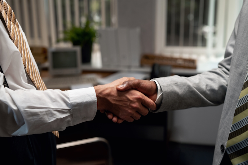 Zwei Männer in Geschäftsanzügen schütteln sich in einem Büro die Hände
